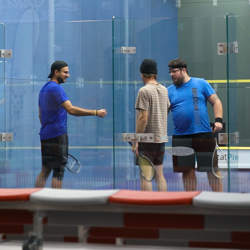 Three males fist-bumping during a squash game
